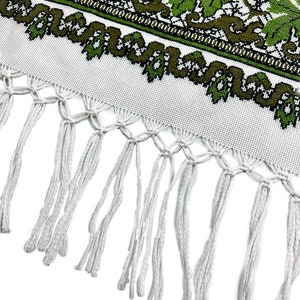 May include: White textile with a green and olive leaf pattern and a fringe. The leaf design is repeated across the top of the textile. The fringe is made of white threads.