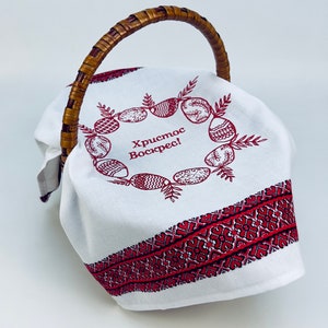May include: White fabric Easter basket with a woven handle. The fabric has a red embroidered border and a wreath of red embroidered eggs with the text "Христос Воскрес!" in the center.