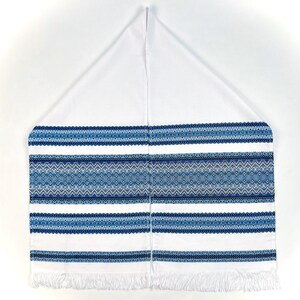 K&ouml;nnte beinhalten: Wei&szlig;-blau bestickter Gebetsschal mit geometrischem Muster. Der Schal hat ein zentrales Band mit aufwendigen blauen Designs, das von horizontalen Streifen und einem Fransenrand begrenzt wird. Der obere Teil ist schlicht wei&szlig;.