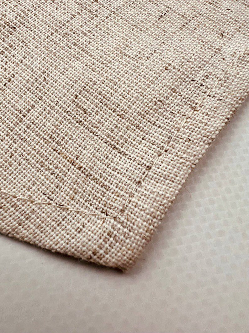 May include: Close-up of a beige fabric with a woven texture. The fabric has a stitched edge.