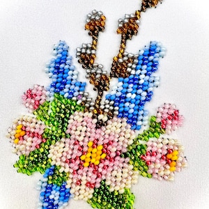 Könnte beinhalten: Ein aufwendiges Blumenmuster aus Perlen in Rosa, Blau, Grün, Gelb und Braun. Die Perlen sind zu Blumen und Blättern angeordnet. Das Kunstwerk ist vor einem weißen Hintergrund platziert, der die filigrane Perlenarbeit hervorhebt.