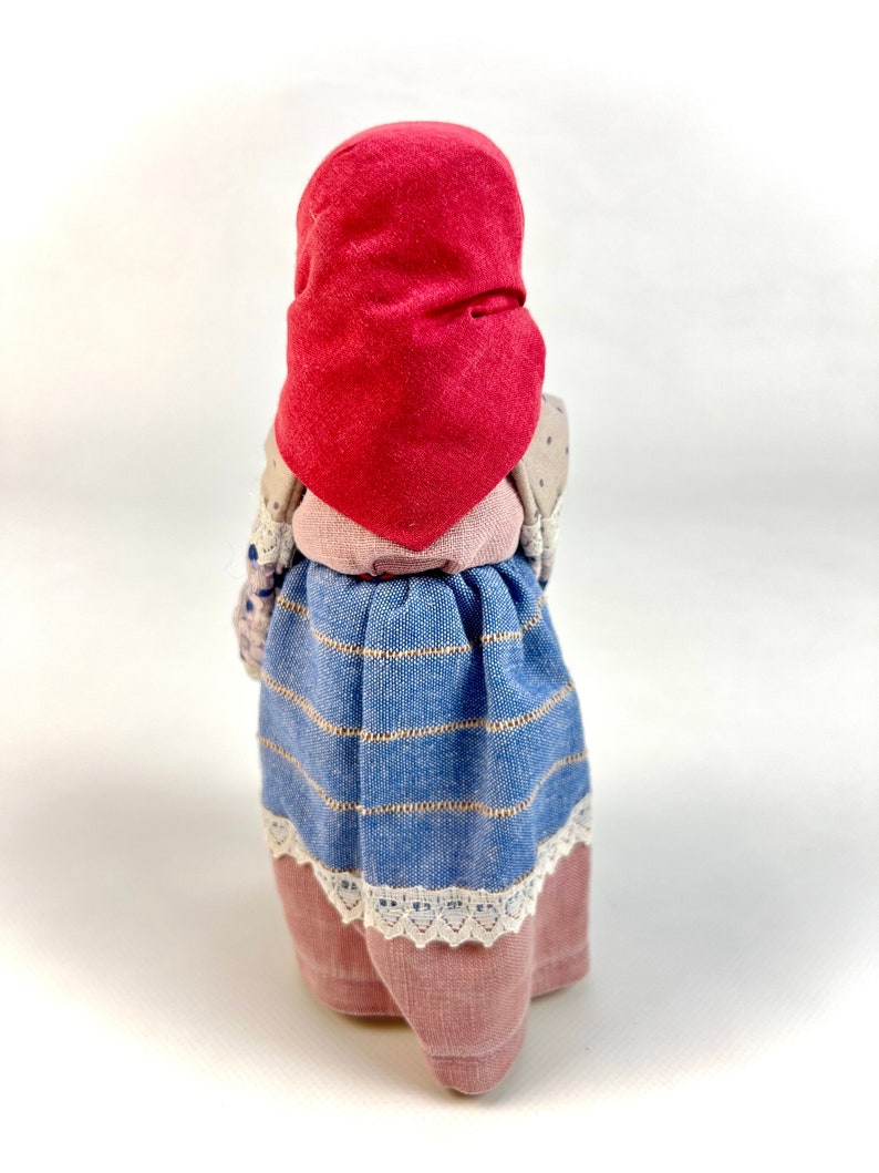 May include: A handmade doll wearing a red bonnet, a blue and white striped skirt, and a pink and white lace trim.