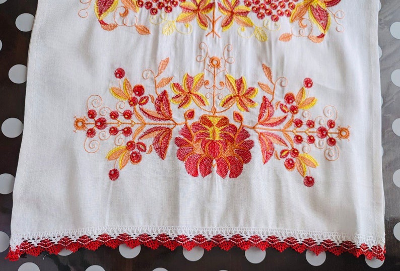 May include: White linen fabric with red and yellow embroidered floral design. The fabric has a red crocheted trim.