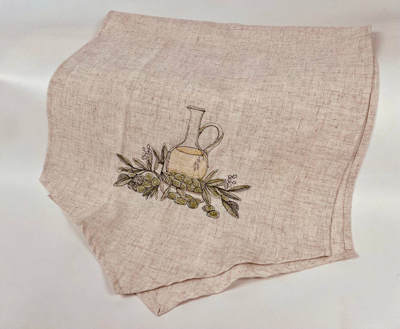 May include: A beige linen kitchen towel with an embroidered design of a green olive branch and a clear glass olive oil bottle.