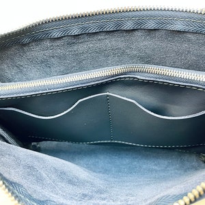 May include: The inside of a black leather bag with a zipper closure. The bag has two interior pockets and a soft, suede-like lining.