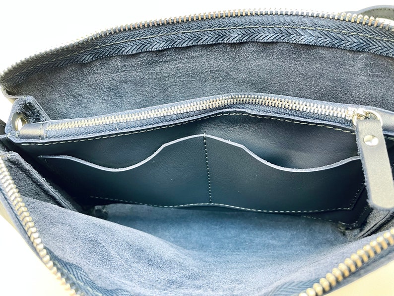 May include: The inside of a black leather bag with a zipper closure. The bag has two interior pockets and a soft, suede-like lining.