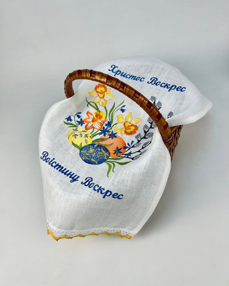 Puede incluir: Forro de cesta de Pascua de lino blanco con narcisos amarillos bordados, huevos azules y amarillos, y el texto "Христос Воскрес" y "Воистину Воскрес".