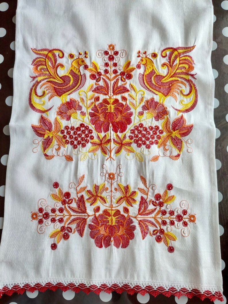 May include: White linen tea towel with red and yellow embroidered birds and floral designs. The towel has a red crocheted trim.