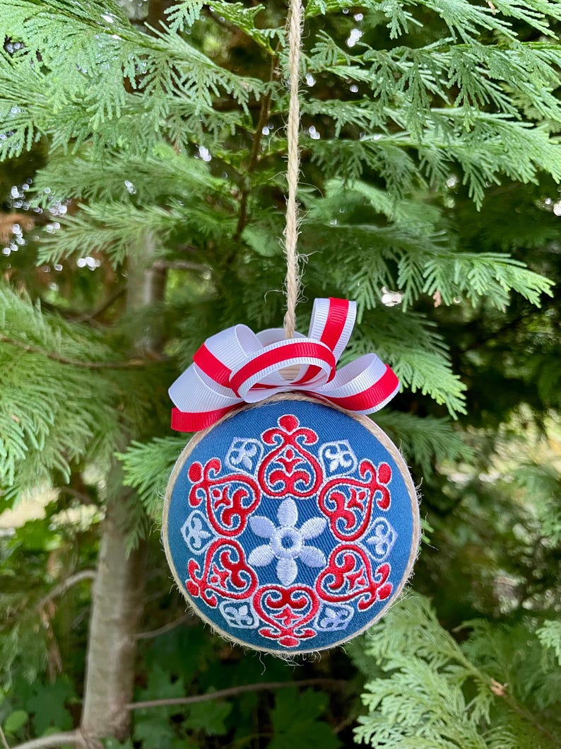 K&ouml;nnte beinhalten: Ein blauer und wei&szlig;er Weihnachtsbaumschmuck mit einem rot-wei&szlig;en Band. Der Schmuck ist mit einem Schneeflockenmuster verziert.