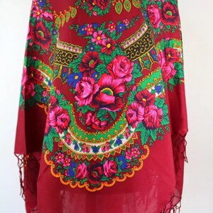 Pu&ograve; includere: Una sciarpa rossa con motivo floreale e bordo a frangia. La sciarpa presenta un design circolare con fiori rosa, rossi, verdi, blu e gialli.