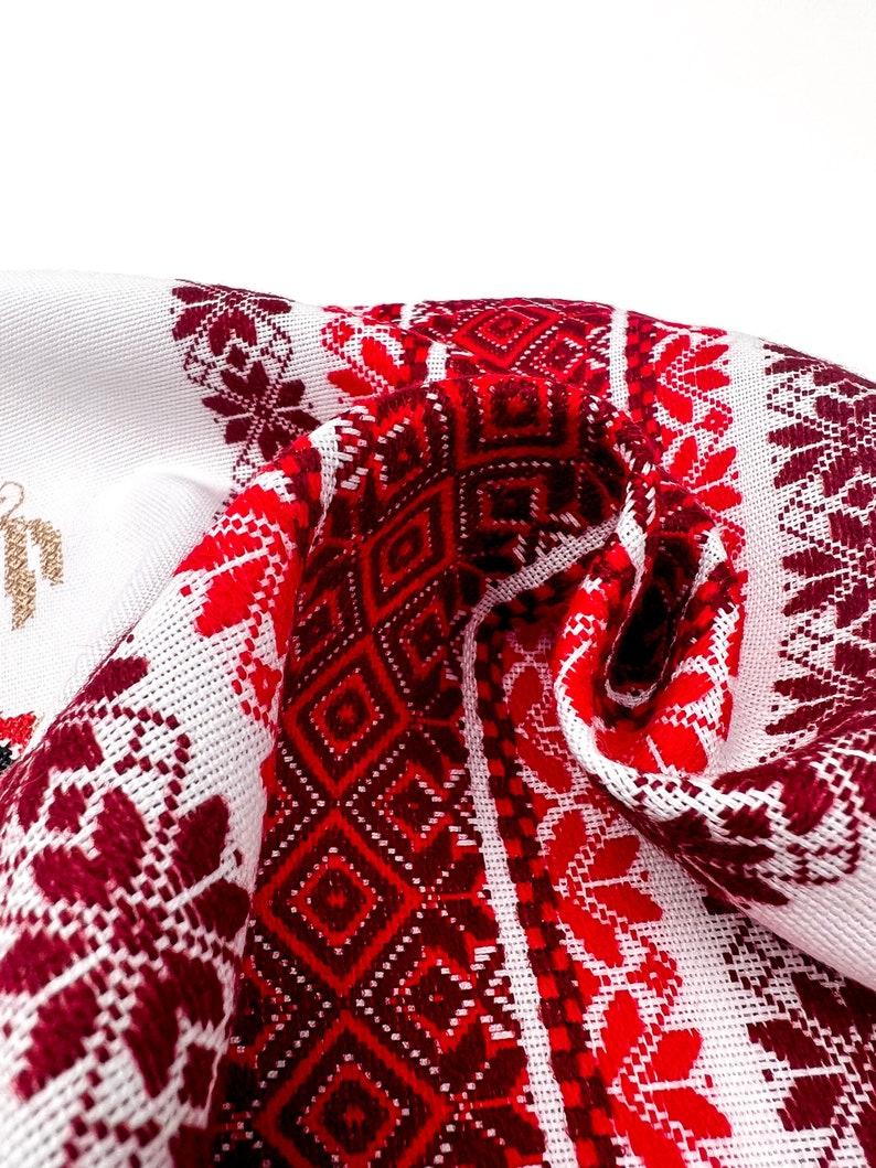 Puede incluir: Tela blanca con un detallado patr&oacute;n bordado en rojo y burdeos. El dise&ntilde;o presenta formas geom&eacute;tricas y motivos florales. La tela est&aacute; doblada, mostrando los intrincados detalles del bordado. El tema general es el arte textil tradicional.