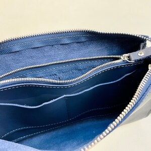 May include: A navy blue leather bag with two zippered compartments and a pocket inside. The bag is open and the interior lining is visible.