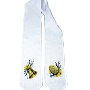 K&ouml;nnte beinhalten: Wei&szlig;er Stoffschal mit gestickten Ostermotiven. Eine Seite zeigt eine goldene Glocke mit gelben Blumen und gr&uuml;nen Zweigen. Die andere Seite hat ein gelbes Ei mit den kyrillischen Buchstaben 'XB' und gelben Blumen.