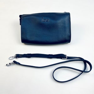 May include: A dark blue leather crossbody bag with a silver strap and a silver clasp. The bag has the word "MAURI" embossed on the front.