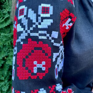 Puede incluir: Camisa de lino negra con patrones florales bordados en rojo y blanco en las mangas.