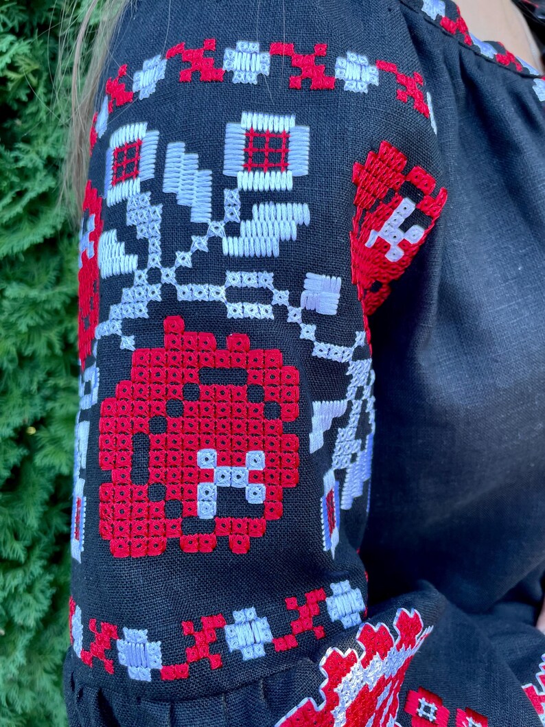 Puede incluir: Camisa de lino negra con patrones florales bordados en rojo y blanco en las mangas.