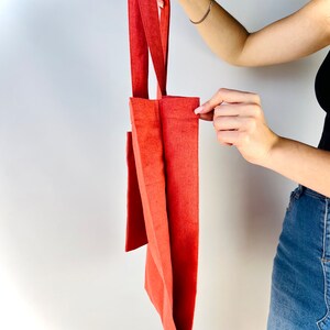 Op de afbeelding: Een rode tote bag gemaakt van canvas met een enkele zak aan de voorkant. De tas heeft twee handvatten.