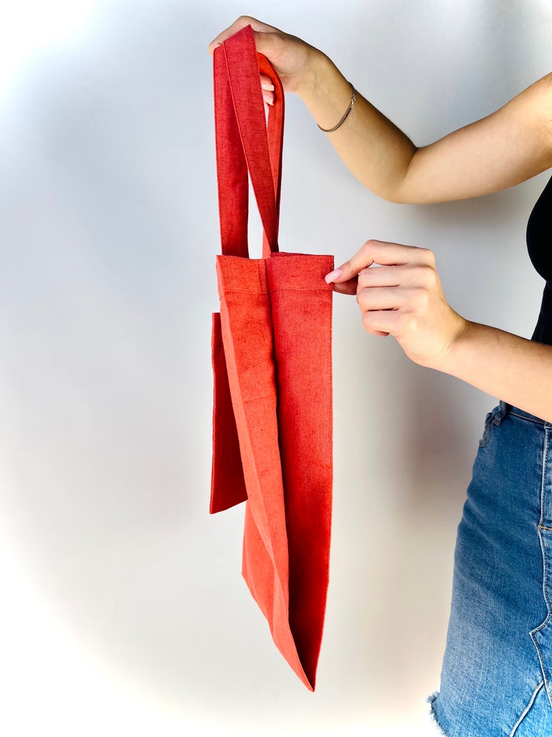Op de afbeelding: Een rode tote bag gemaakt van canvas met een enkele zak aan de voorkant. De tas heeft twee handvatten.