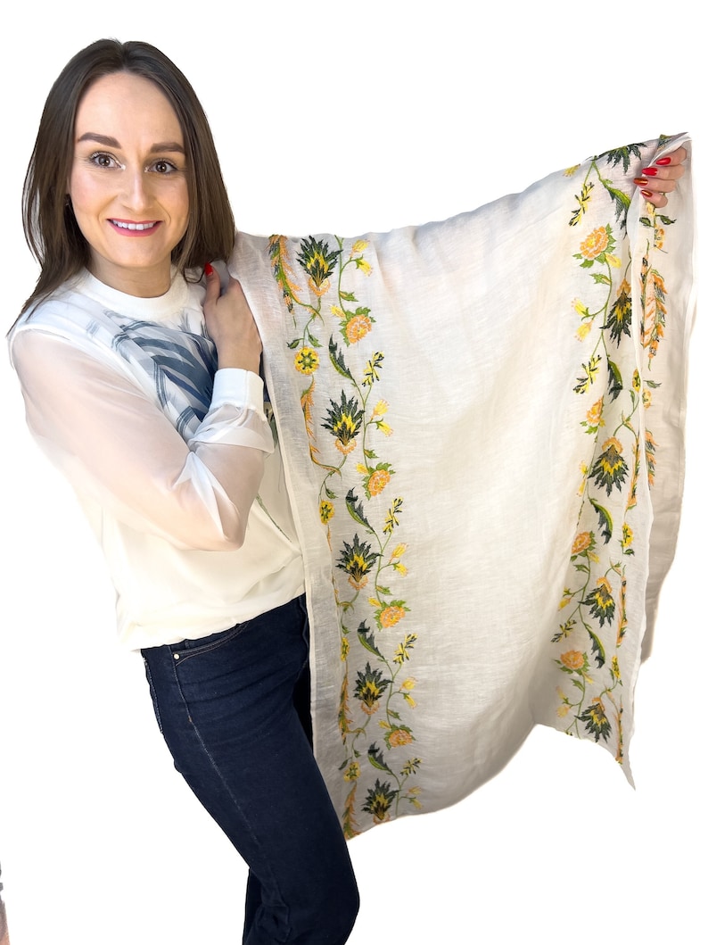 Puede incluir: Una bufanda blanca con un borde floral en tonos amarillos y verdes. La bufanda est&aacute; hecha de una tela ligera y es perfecta para agregar un toque de elegancia a cualquier atuendo.