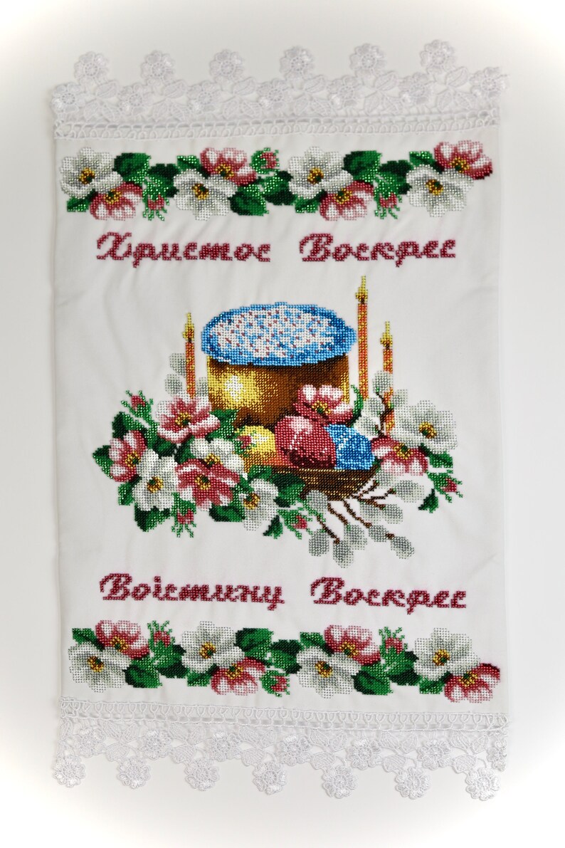 K&ouml;nnte beinhalten: Bestickter wei&szlig;er Stoff mit floralen und religi&ouml;sen Motiven. Das Design zeigt einen goldbraunen Kuchen mit blauen Streuseln, umgeben von Blumen, Kerzen und Ostereiern. Der Text "Christus ist auferstanden" und "Wahrlich, er ist auferstanden" ist rot gestickt.