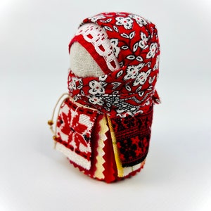 Op de afbeelding: Een traditionele Russische volkspop, bekend als een nestpop of matrjosjka, is gemaakt van stof en versierd met rode en witte bloemenpatronen. De pop is gewikkeld in een rode en witte gebloemde stoffen hoofddoek.