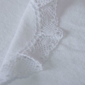 May include: White fabric with a white lace trim. The lace is delicate and intricate.