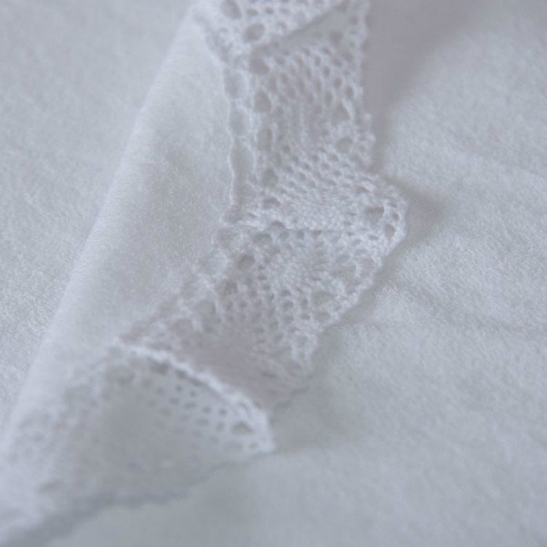 May include: White fabric with a white lace trim. The lace is delicate and intricate.
