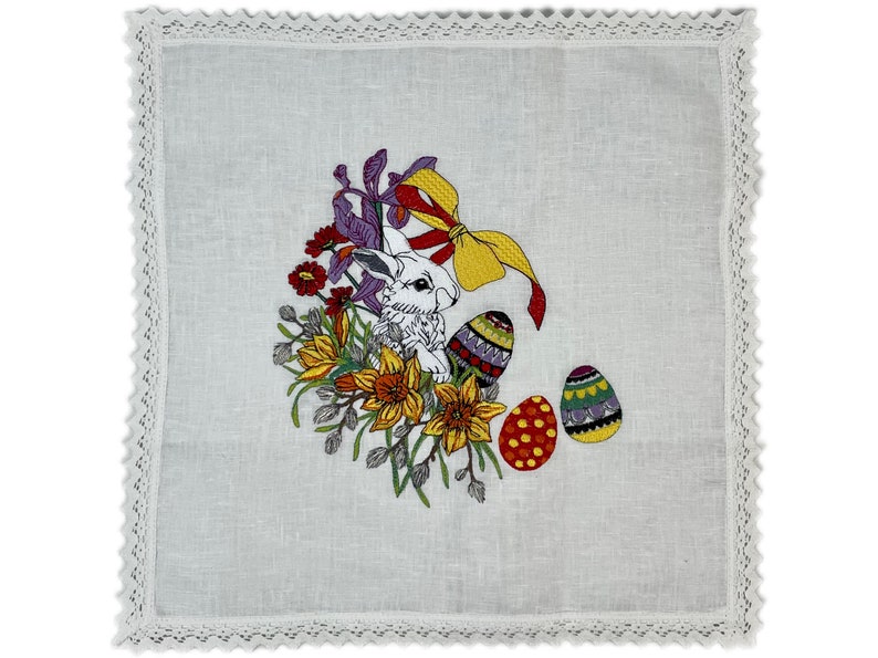 May include: White linen tea towel with embroidered Easter bunny, flowers, and eggs. The bunny is surrounded by yellow daffodils, purple irises, and red flowers. The eggs are decorated with colorful patterns.