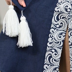 May include: A navy blue linen dress with white embroidered details and white tassel accents.