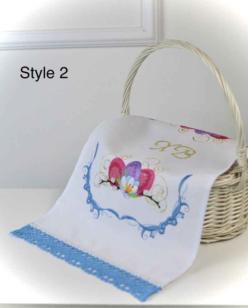 May include: A white woven basket holds a white cloth with embroidered flowers in pink, purple, and blue. The cloth has a blue lace trim. The text "Style 2" is in the upper left corner.