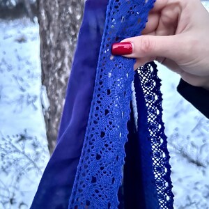 May include: A close-up of a blue fabric with a lace trim. The fabric is held in a hand with red nail polish.
