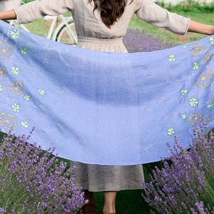 Pode incluir: Um len&ccedil;o azul claro com um padr&atilde;o floral de dentes-de-le&atilde;o amarelos e verdes. O len&ccedil;o &eacute; segurado na frente de um campo de lavanda.