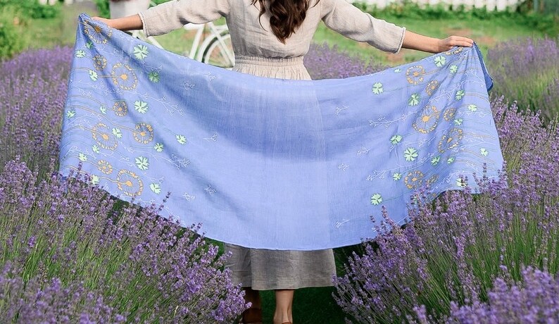 Pode incluir: Um len&ccedil;o azul claro com um padr&atilde;o floral de dentes-de-le&atilde;o amarelos e verdes. O len&ccedil;o &eacute; segurado na frente de um campo de lavanda.