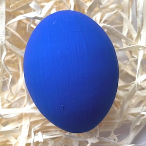 May include: A vibrant blue egg with a textured finish, set against a backdrop of light-coloured shredded paper. The egg's bold colour provides a striking contrast to the neutral background. The egg is likely a decorative item.
