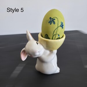 May include: A white ceramic bunny figurine holding a yellow bowl with a green egg inside. The egg is decorated with blue floral designs. The text "Style 5" is in the upper left corner. Easter decor.