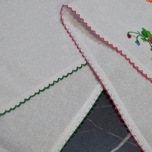 Puede incluir: Dos cuadrados de tela blanca con bordes festoneados. Un cuadrado tiene un borde verde y el otro un borde rosa.