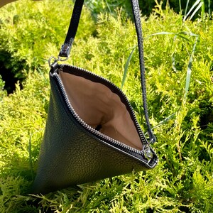 May include: A black leather triangular shaped clutch bag with a zipper closure and a long strap.