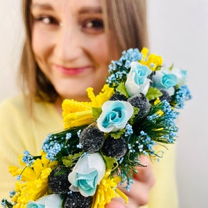 Pode incluir: Uma faixa de cabe&ccedil;a floral com flores azuis e amarelas, folhas verdes e bagas pretas. A faixa de cabe&ccedil;a &eacute; feita de tecido e arame.