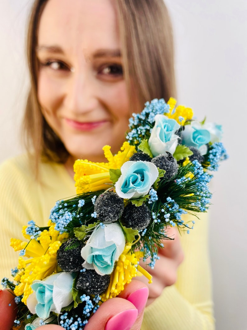 Pode incluir: Uma faixa de cabe&ccedil;a floral com flores azuis e amarelas, folhas verdes e bagas pretas. A faixa de cabe&ccedil;a &eacute; feita de tecido e arame.