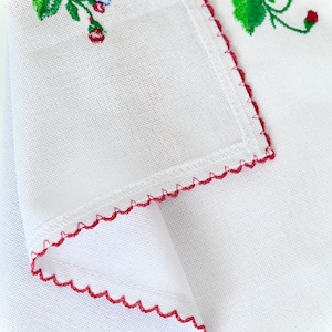 Pode incluir: Tecido branco com uma borda bordada vermelha e um desenho floral em vermelho, verde e azul.