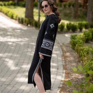 Pode incluir: Vestido longo de linho preto com padr&otilde;es geom&eacute;tricos bordados em branco e cinza nas mangas e no corpete. O vestido tem uma fenda alta e &eacute; usado com t&ecirc;nis brancos e cinza. O vestido &eacute; longo maxi.