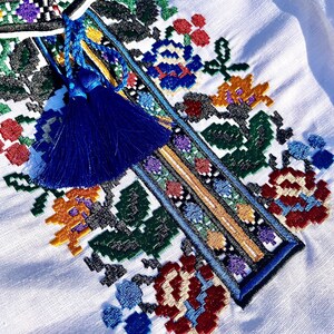May include: White linen shirt with a colorful embroidered floral design and a blue tassel.