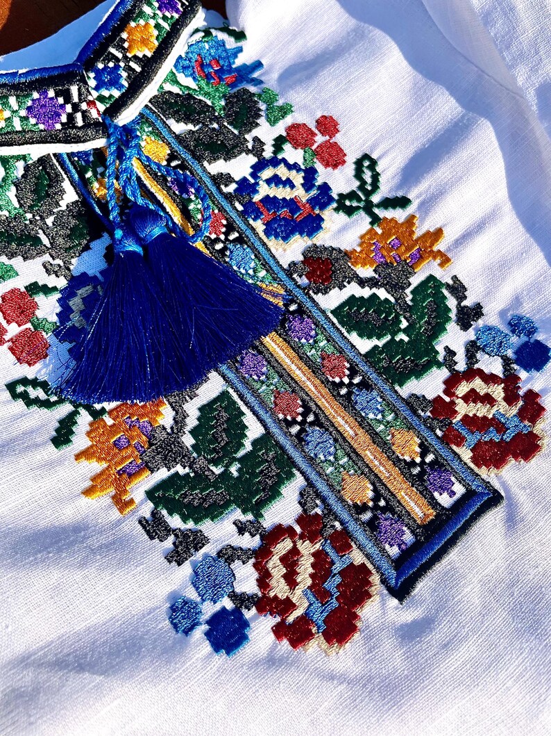 May include: White linen shirt with a colorful embroidered floral design and a blue tassel.