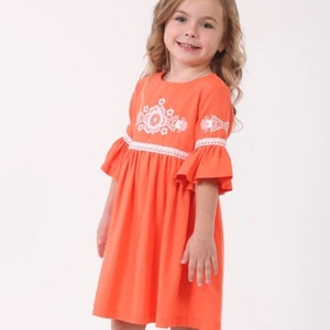 K&ouml;nnte beinhalten: Ein junges M&auml;dchen tr&auml;gt ein leuchtend oranges Kleid mit wei&szlig;en gestickten Blumen und einer wei&szlig;en Spitzenborte. Das Kleid hat einen leicht ausgestellten Rock und kurze &Auml;rmel.