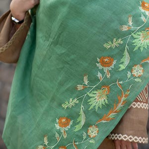 May include: A green shawl with embroidered floral designs in shades of orange, white, and green.