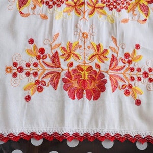 Peut inclure: Textile en lin blanc avec broderies vibrantes de motifs floraux et de baies rouges, oranges et jaunes. Le bord inf&eacute;rieur est orn&eacute; d'une bordure en dentelle rouge d&eacute;corative. La broderie est d&eacute;taill&eacute;e.