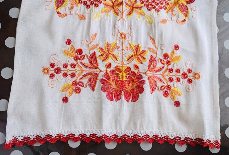 Peut inclure: Textile en lin blanc avec broderies vibrantes de motifs floraux et de baies rouges, oranges et jaunes. Le bord inf&eacute;rieur est orn&eacute; d'une bordure en dentelle rouge d&eacute;corative. La broderie est d&eacute;taill&eacute;e.
