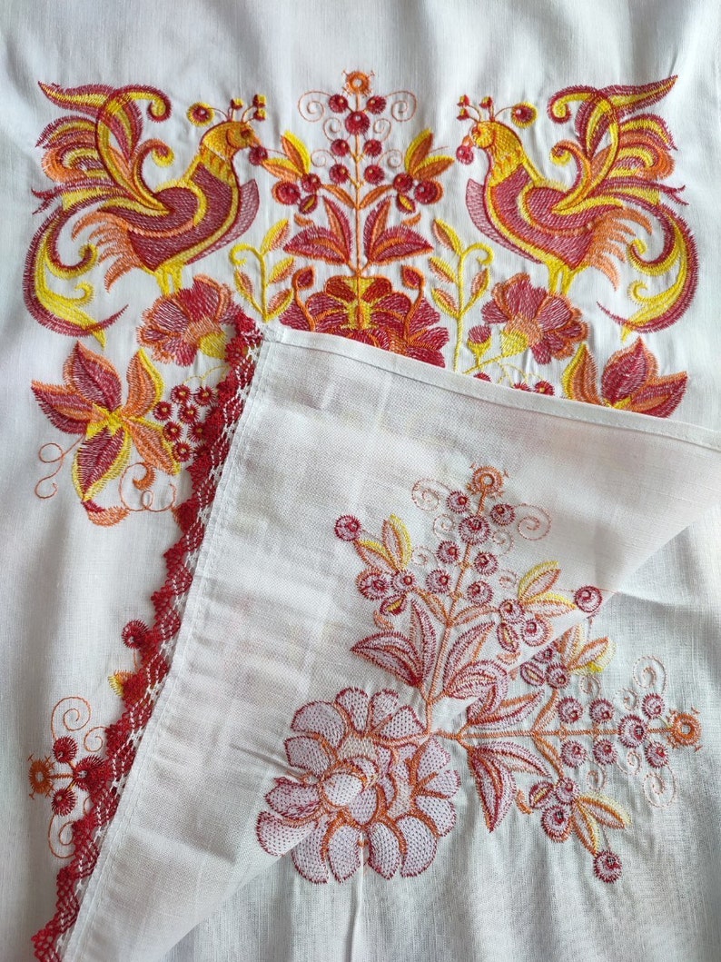 May include: White fabric with red and yellow embroidered flowers and birds. The fabric has a lace trim.