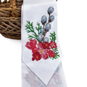 May include: White fabric with a beaded embroidery design of red flowers, green leaves, and grey willow branches. The fabric is folded and draped over a wicker basket.