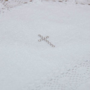 May include: A white fabric with a small silver cross made of rhinestones.